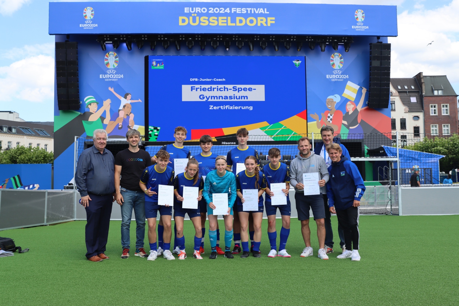 [{"clang_id":1,"value":"Gruppe Jugendlicher mit Zertifikaten vor einer LED-Wand mit EURO 2024 Logo und dem Text \"DFB-Junior-Coach, Friedrich-Spee-Gymnasium, Zertifizierung\". Zwei erwachsene Begleiter."}]