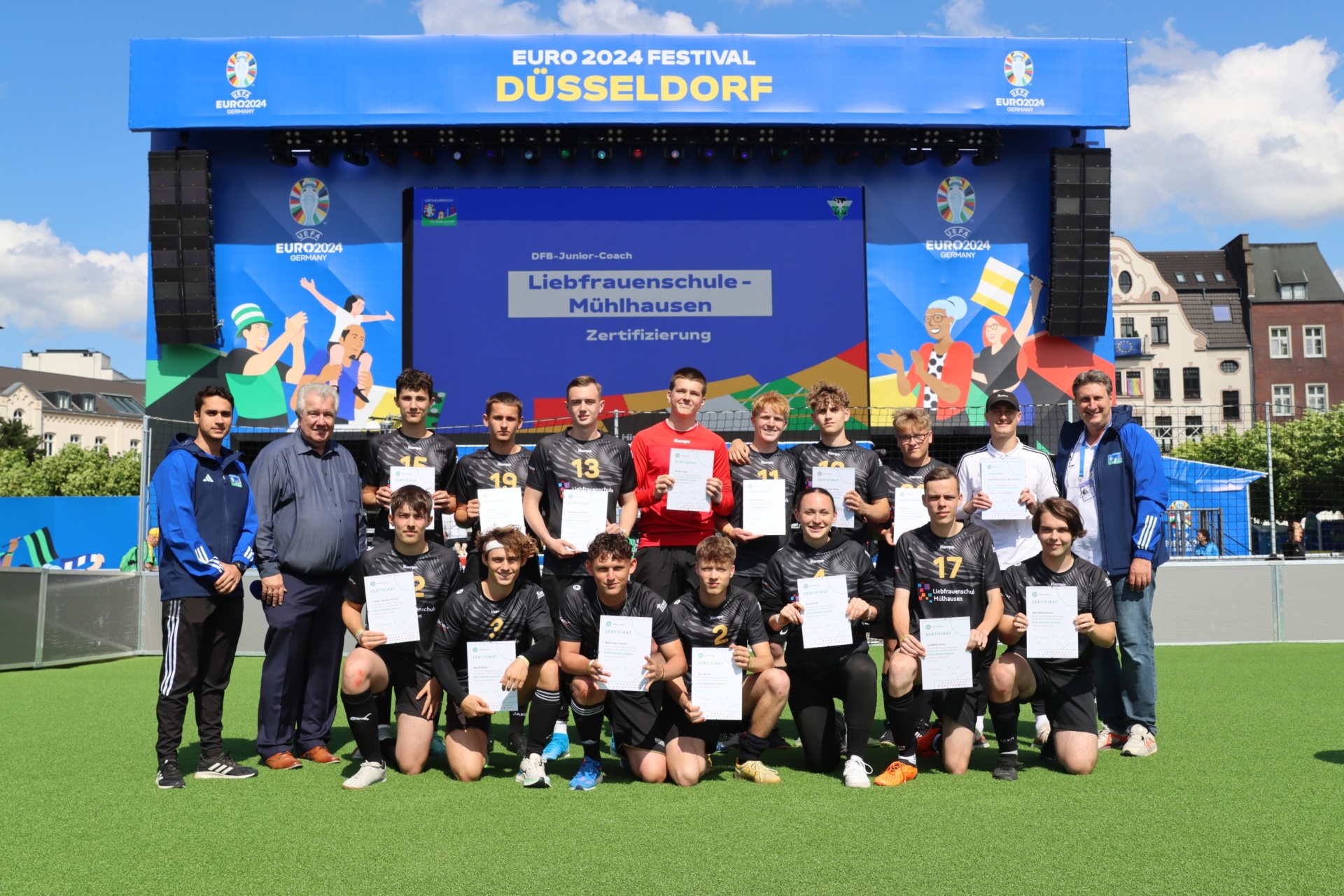 [{"clang_id":1,"value":"Gruppe Jugendlicher mit Zertifikaten vor Banner \"EURO 2024 Festival Düsseldorf\". Männer stehen seitlich als Betreuer dabei. Fußballfeld im Hintergrund."}]