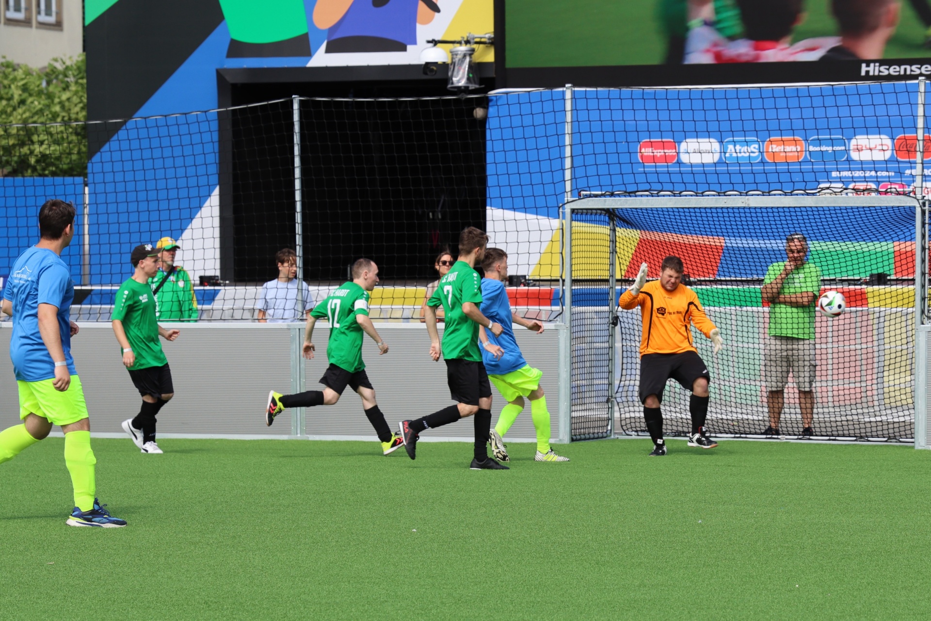 [{"clang_id":1,"value":"Fußballspiel. Spieler in grünen Trikots greifen einen Ball an, während der Torwart versucht, ihn zu verteidigen. Im Hintergrund Banner und Zuschauertribüne."}]