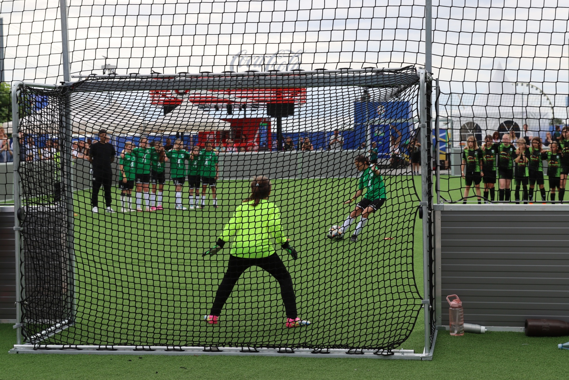 [{"clang_id":1,"value":"Fußballtor mit Netz im Vordergrund. Torwartin in grüner Ausrüstung, Gegenspielerin mit Ball. Im Hintergrund weitere Fußballspielerinnen und Zuschauer."}]