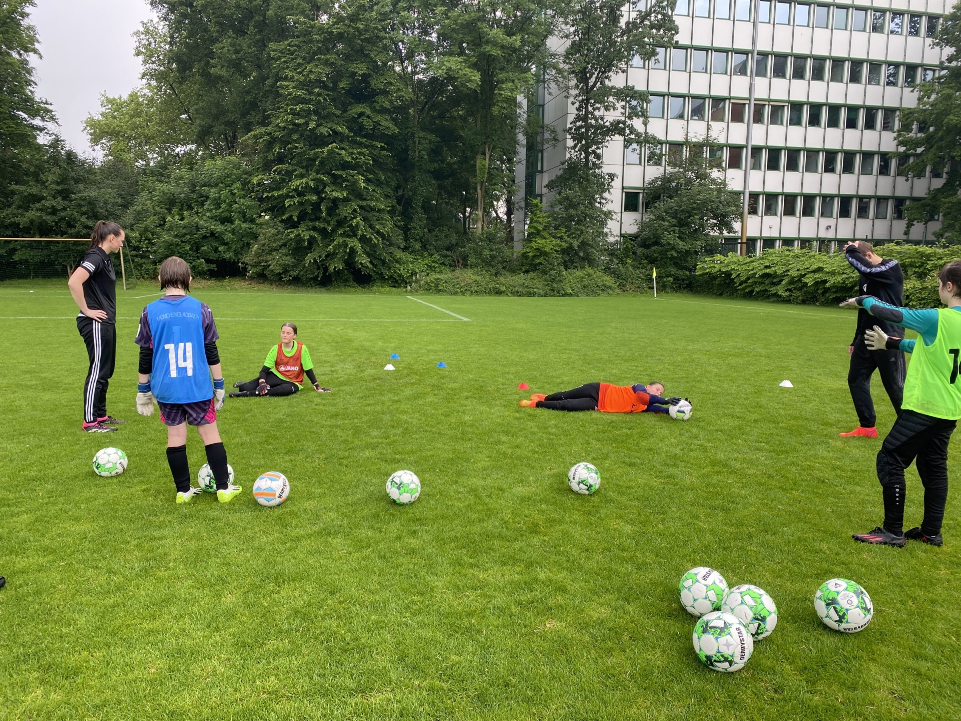 [{"clang_id":1,"value":"Fußballtraining: Gruppe Jugendlicher und Trainer auf Rasenfeld. Mehrere liegen am Boden, andere stehen und üben mit Fußbällen. Im Hintergrund Gebäude und Bäume."}]