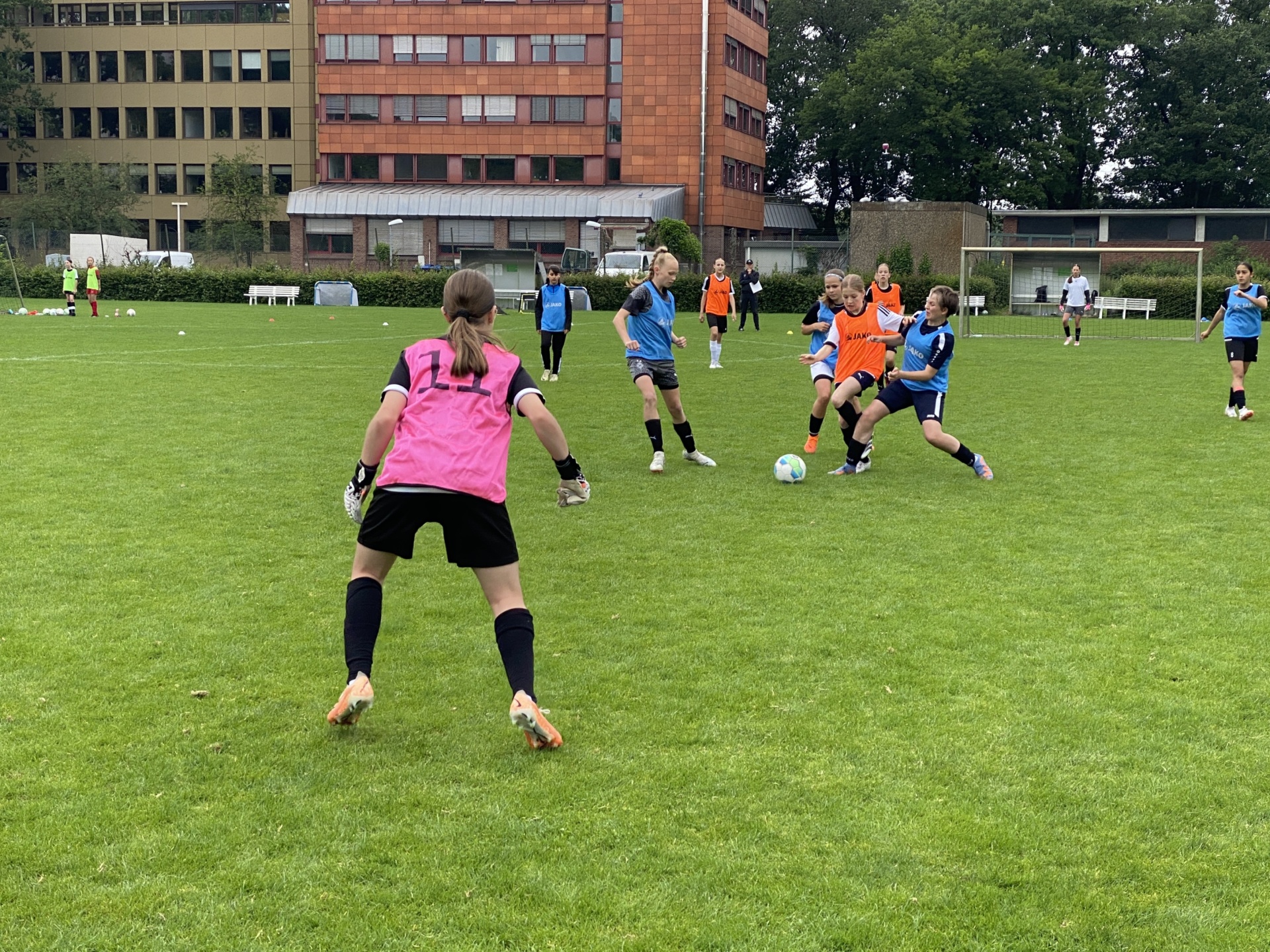 [{"clang_id":1,"value":"Fußballspiel mit mehreren Kindern auf einem grünen Rasenfeld. Im Hintergrund ein mehrstöckiges Gebäude."}]