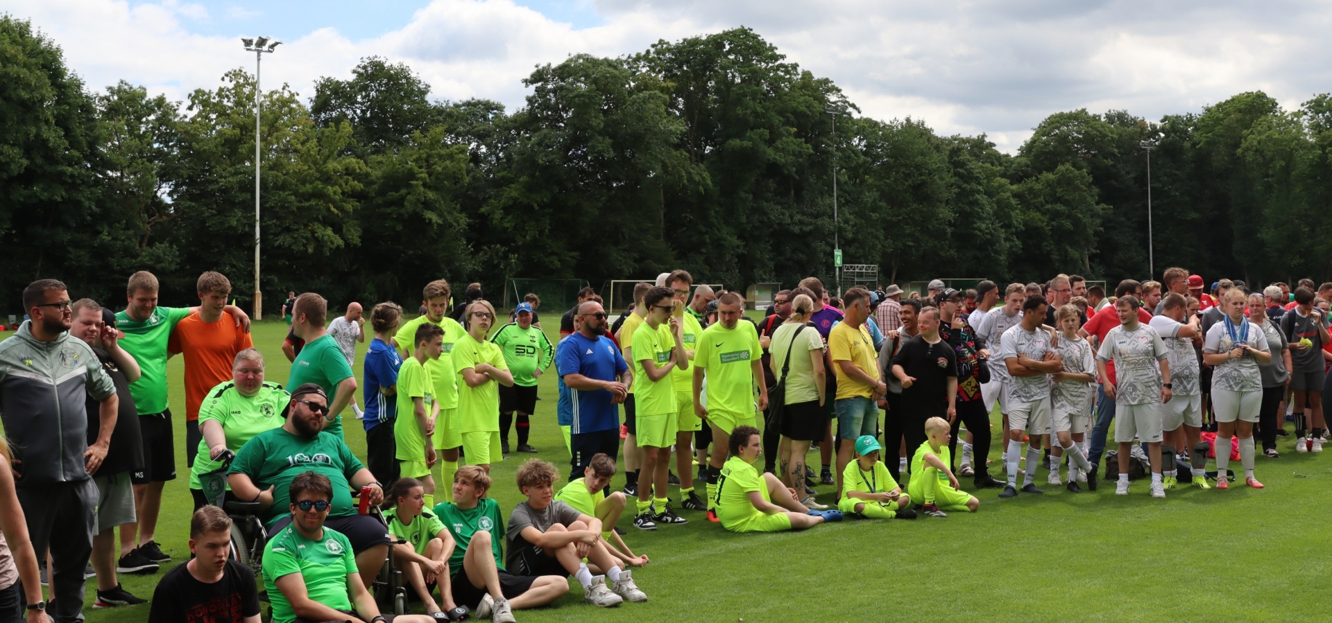 [{"clang_id":1,"value":"Fußballplatz mit zwei Mannschaften in grünen und weißen Trikots, die sich nach einem Spiel gegenüberstehen. Zuschauer im Hintergrund, Bäume und leichter Himmel."}]