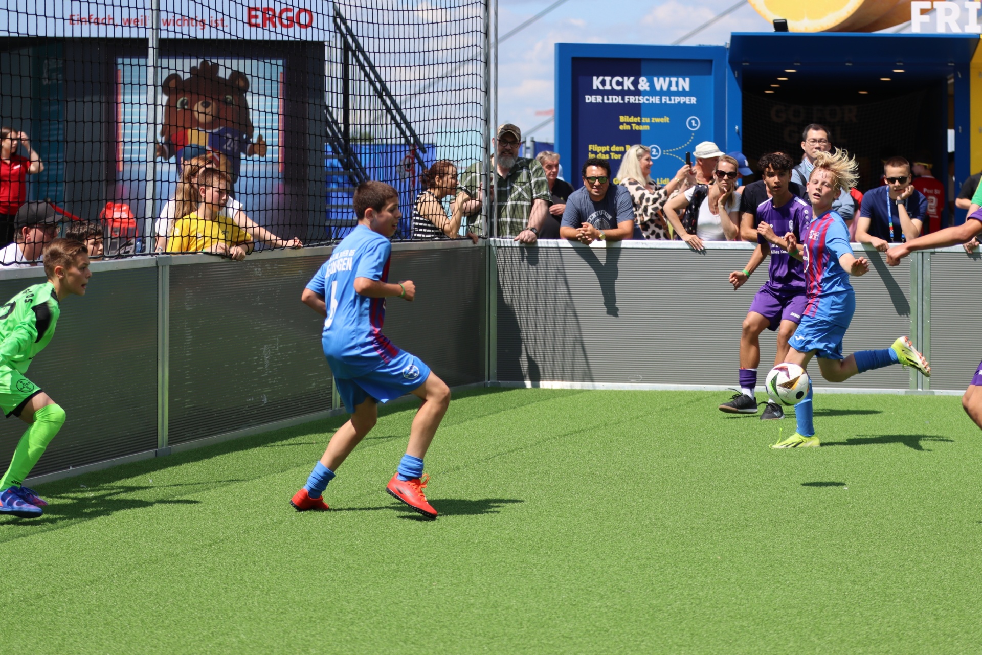 [{"clang_id":1,"value":"Fußballspiel mit Kindern auf Kunstgrün. Zwei Spieler im Fokus, Hintergrund mit Zuschauern und Werbebanner."}]