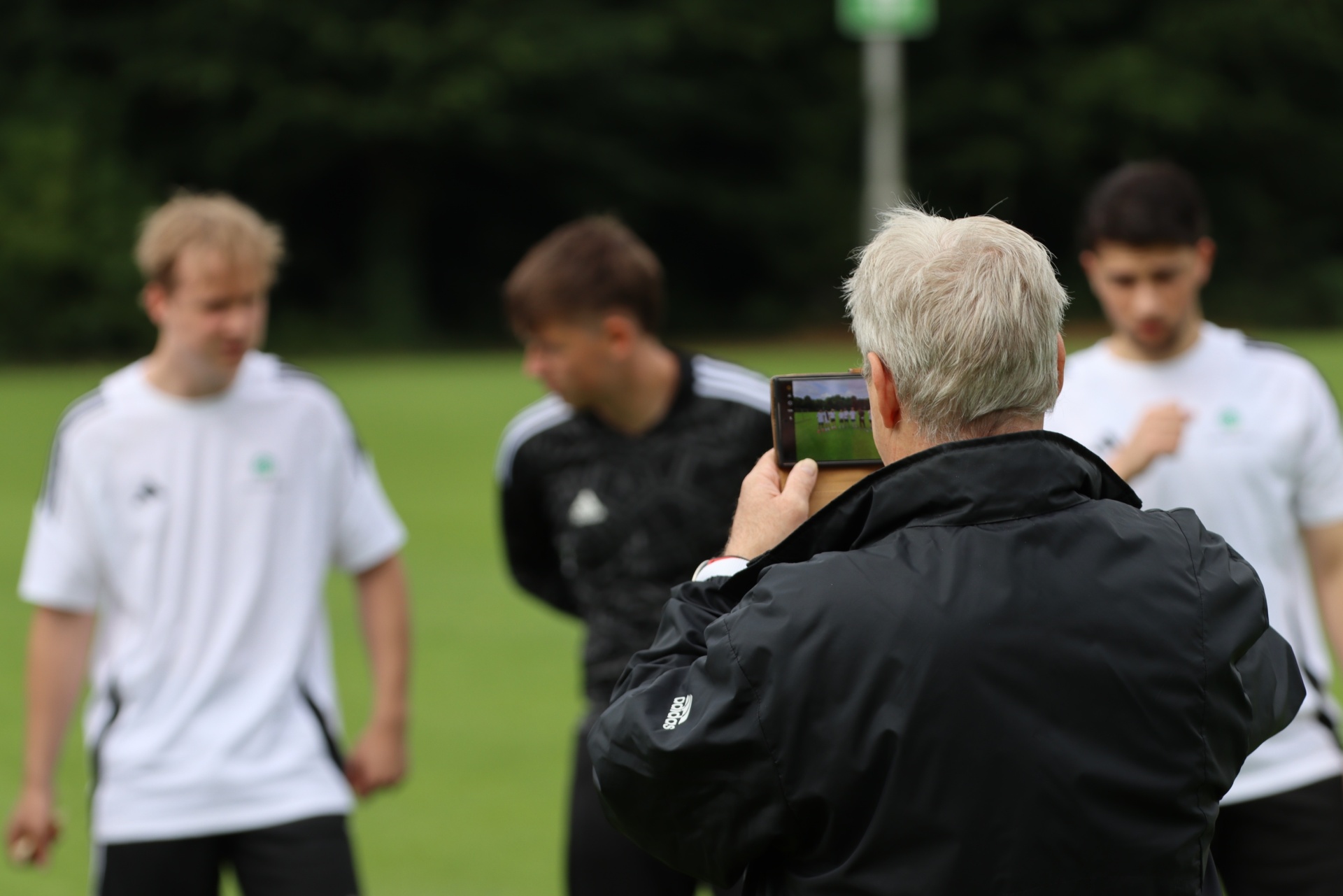 [{"clang_id":1,"value":"Fußballfeld: Trainer mit grauem Haar fotografiert vier junge Fußballspieler in Trainingsanzügen mit dem Smartphone."}]
