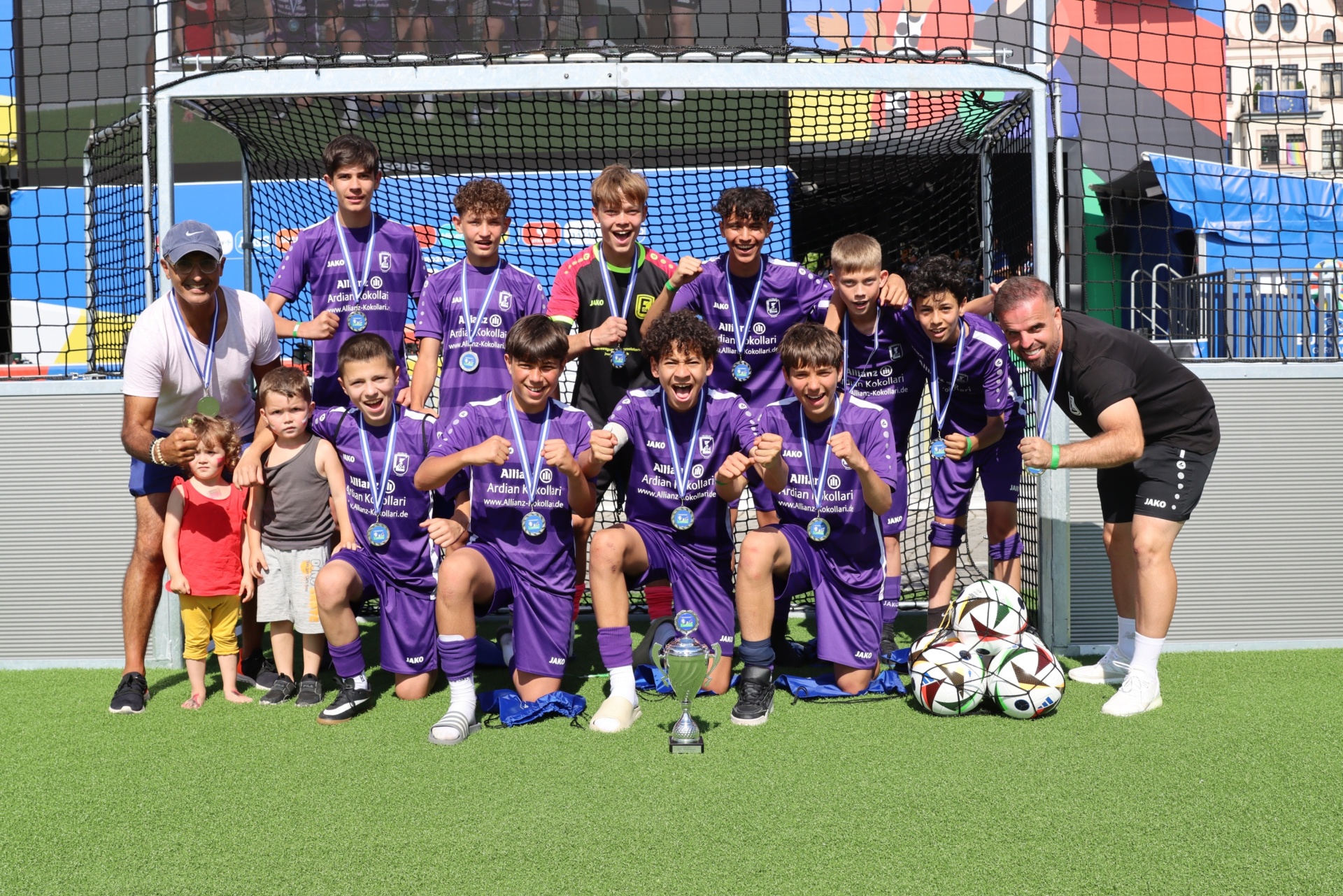 [{"clang_id":1,"value":"Fußballmannschaft mit Trainern und Kindern in violetten Trikots vor einem Fußballtor. Alle tragen Medaillen um den Hals."}]