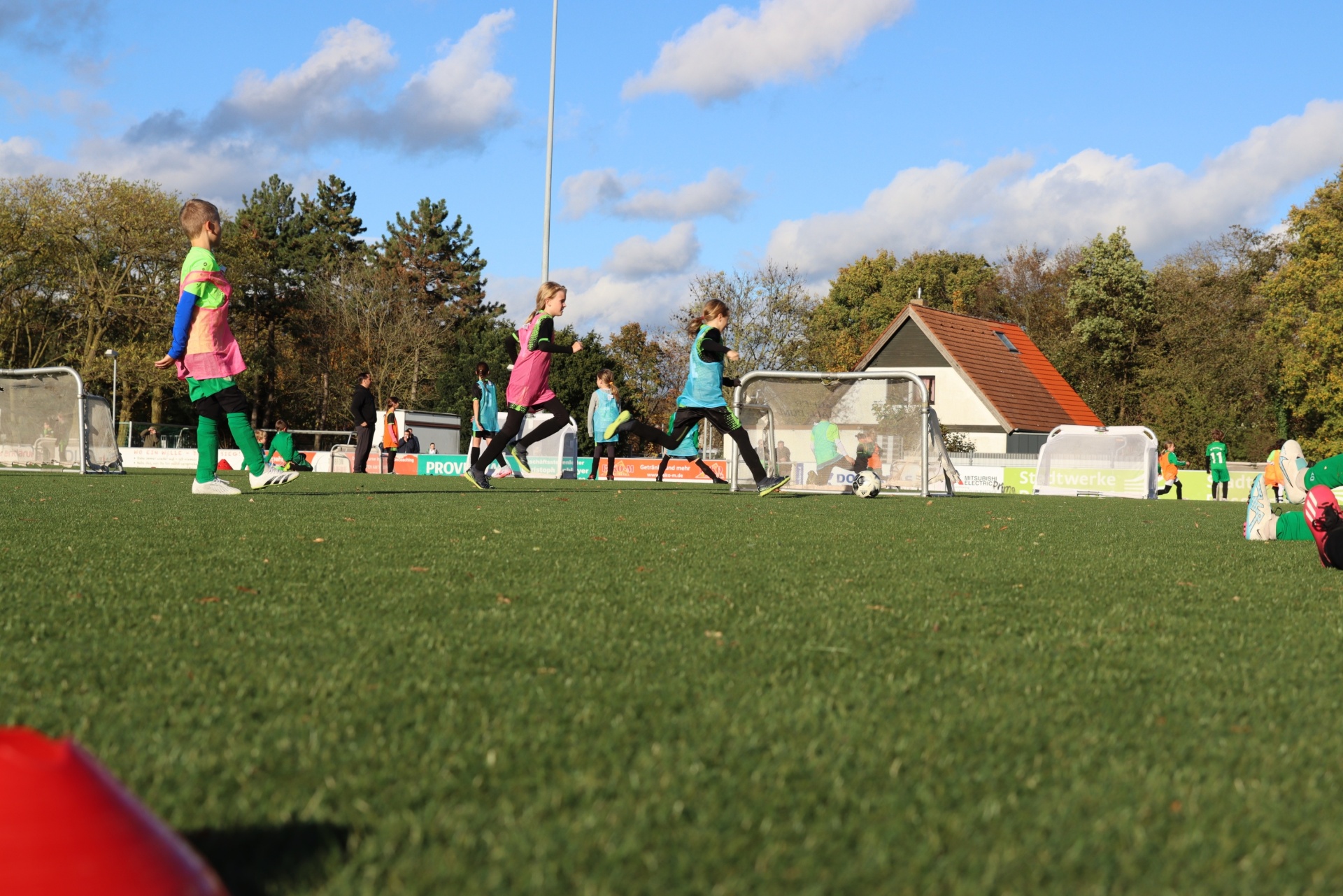 [{"clang_id":1,"value":"Fußballfeld mit Kindern beim Laufen. Im Hintergrund Gebäude und Bäume unter blauem Himmel mit Wolken."}]