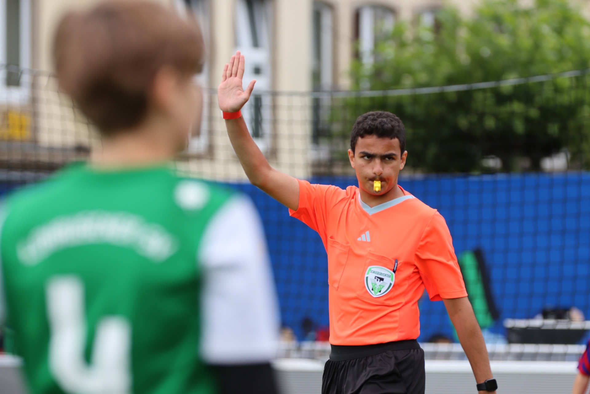 [{"clang_id":1,"value":"Fußball-Schiedsrichter mit hochgehobener Hand signalisiert Abseits. Spieler mit grünem Trikot im Hintergrund. Stadionatmosphäre."}]