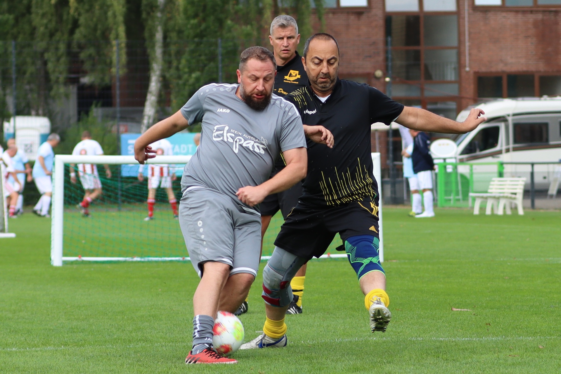[{"clang_id":1,"value":"Zwei Fußballspieler kämpfen um den Ball auf einem grünen Rasenplatz. Links ein Spieler in grau, rechts in schwarz-gelb. Im Hintergrund Zuschauer und Bäume."}]