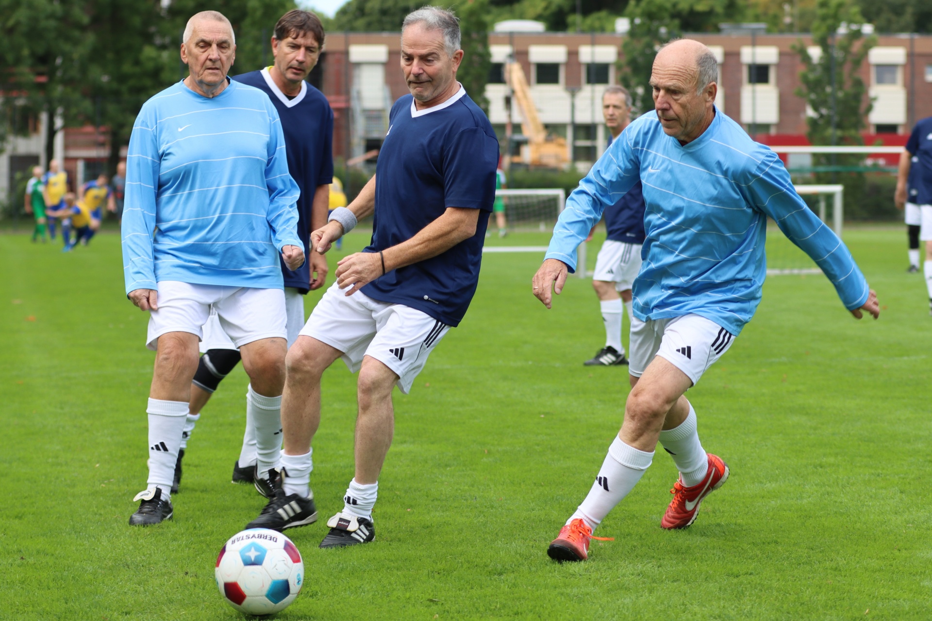[{"clang_id":1,"value":"Vier ältere Männer spielen Fußball auf einem grünen Rasen. Zwei tragen hellblaue, zwei dunkelblaue Sportkleidung. Ein Fußball liegt auf dem Boden."}]