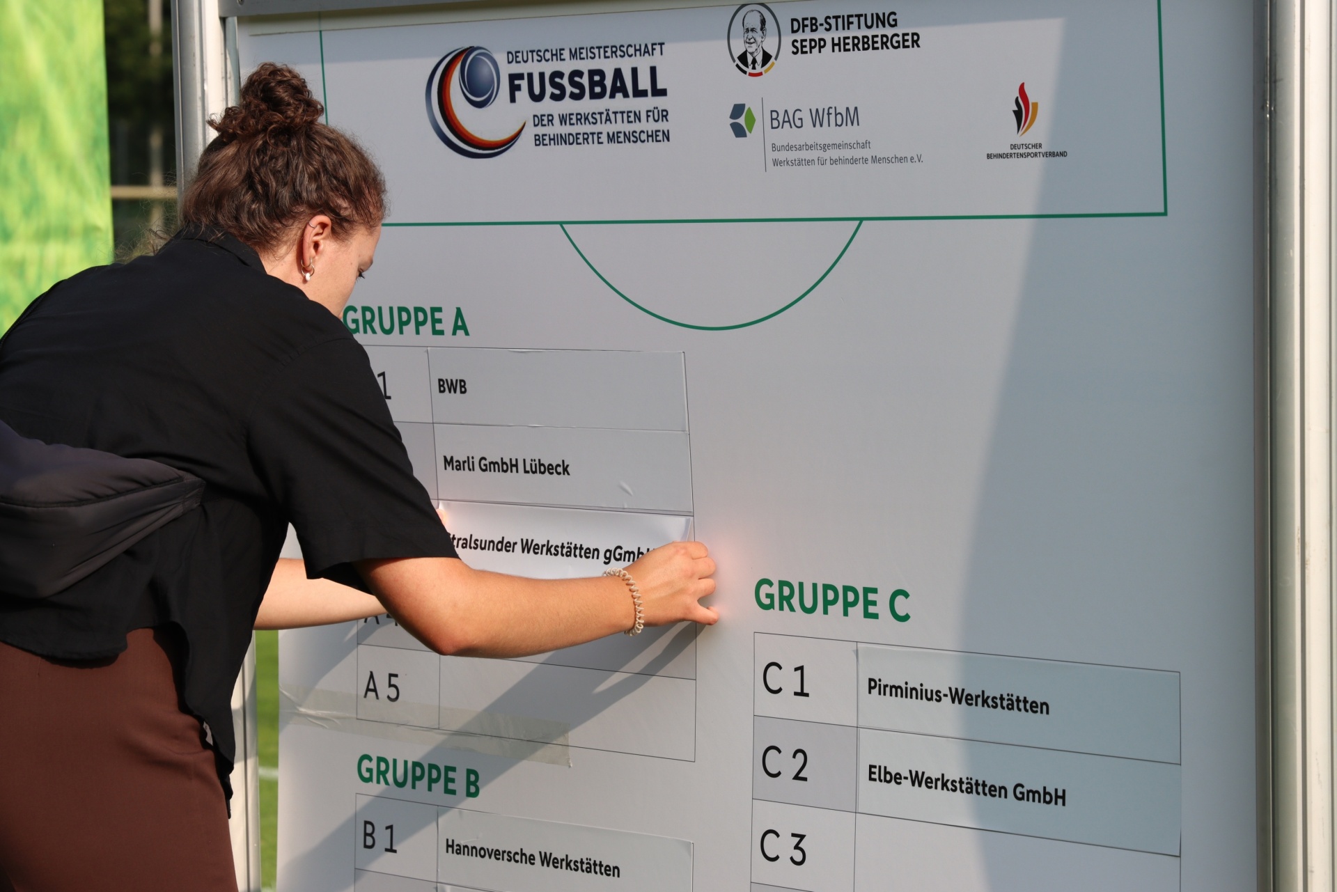 [{"clang_id":1,"value":"Mann mit schwarzem Shirt und weißen Cap markiert auf einem Whiteboard Gruppeneinteilungen für eine Fußball-Meisterschaft für Menschen mit Behinderung."}]