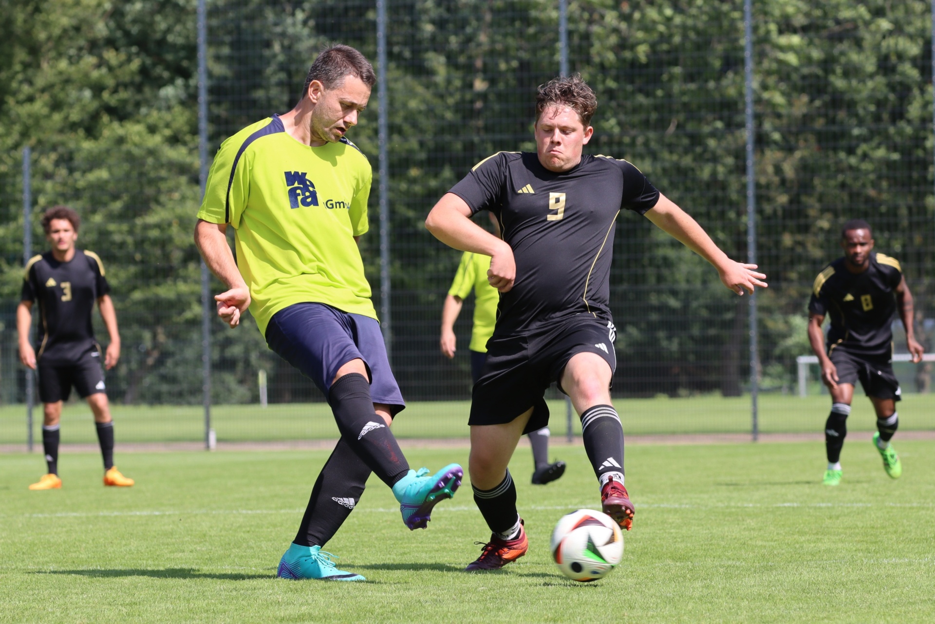 [{"clang_id":1,"value":"Fußballspieler auf grünem Rasen. Zwei Spieler im Vordergrund bei Ballaktion, weitere Spieler im Hintergrund. Tragen Trikots und Shorts."}]