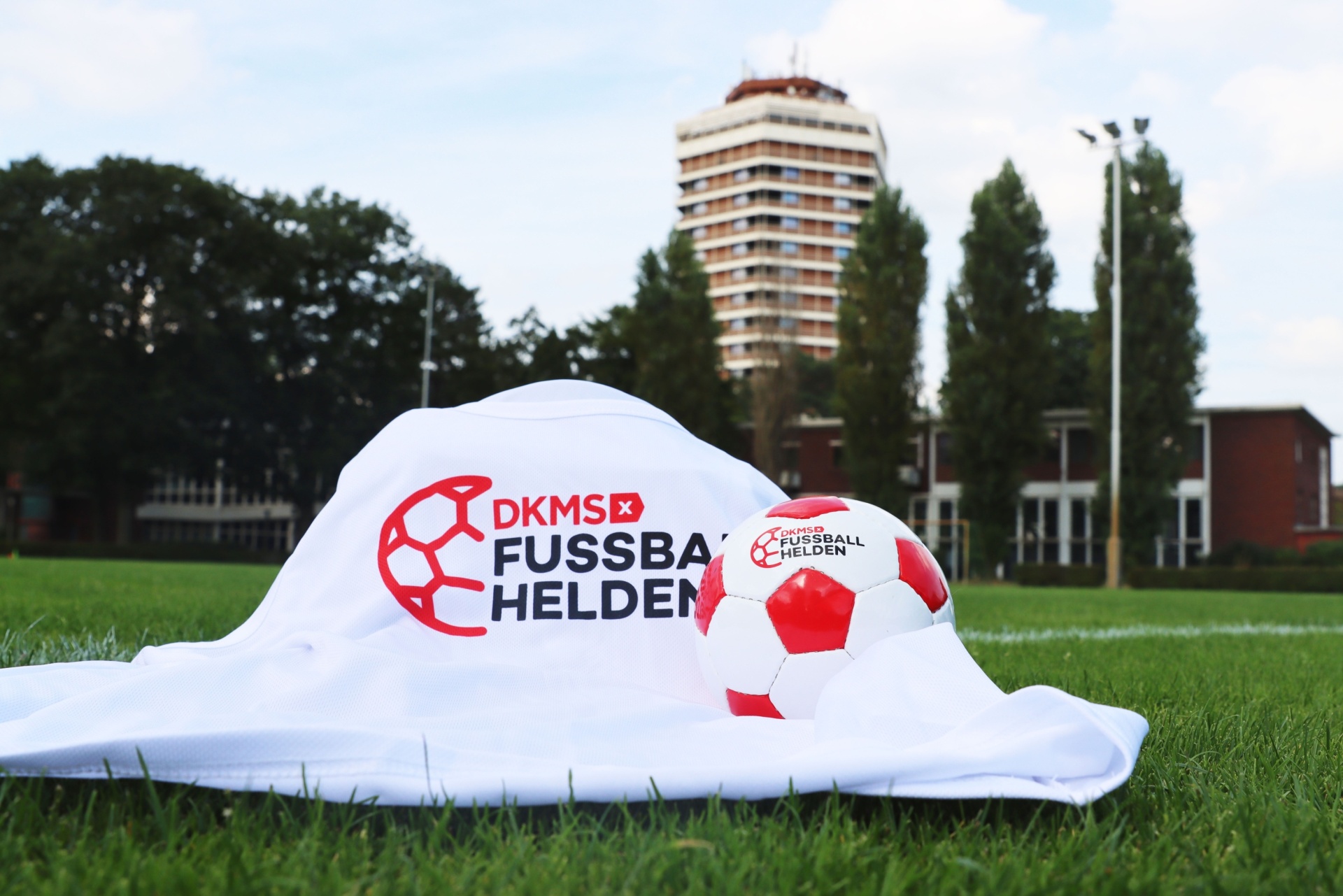 [{"clang_id":1,"value":"Fußball auf Rasen: Ein Fußball unter einem weißen Tuch mit rotem \"DKMS FUSSBALLHELDEN\"-Logo. Im Hintergrund Gebäude und Bäume."}]