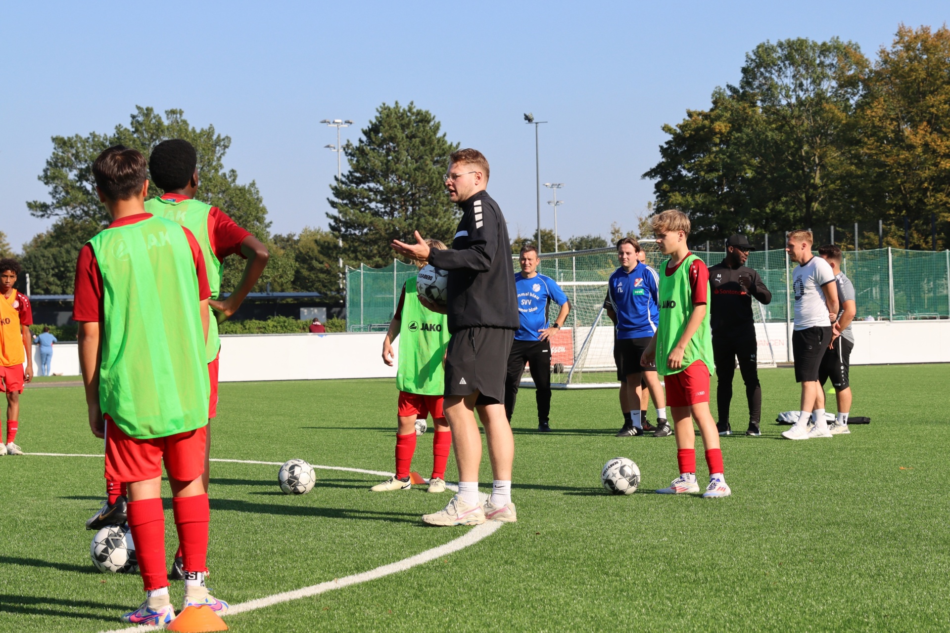 [{"clang_id":1,"value":"Fußballtrainer erklärt Taktik an Jugendspieler auf Kunstrasenfeld. Spieler tragen Trainingswesten und Vereinskleidung. Im Hintergrund Gebäude und Bäume."}]