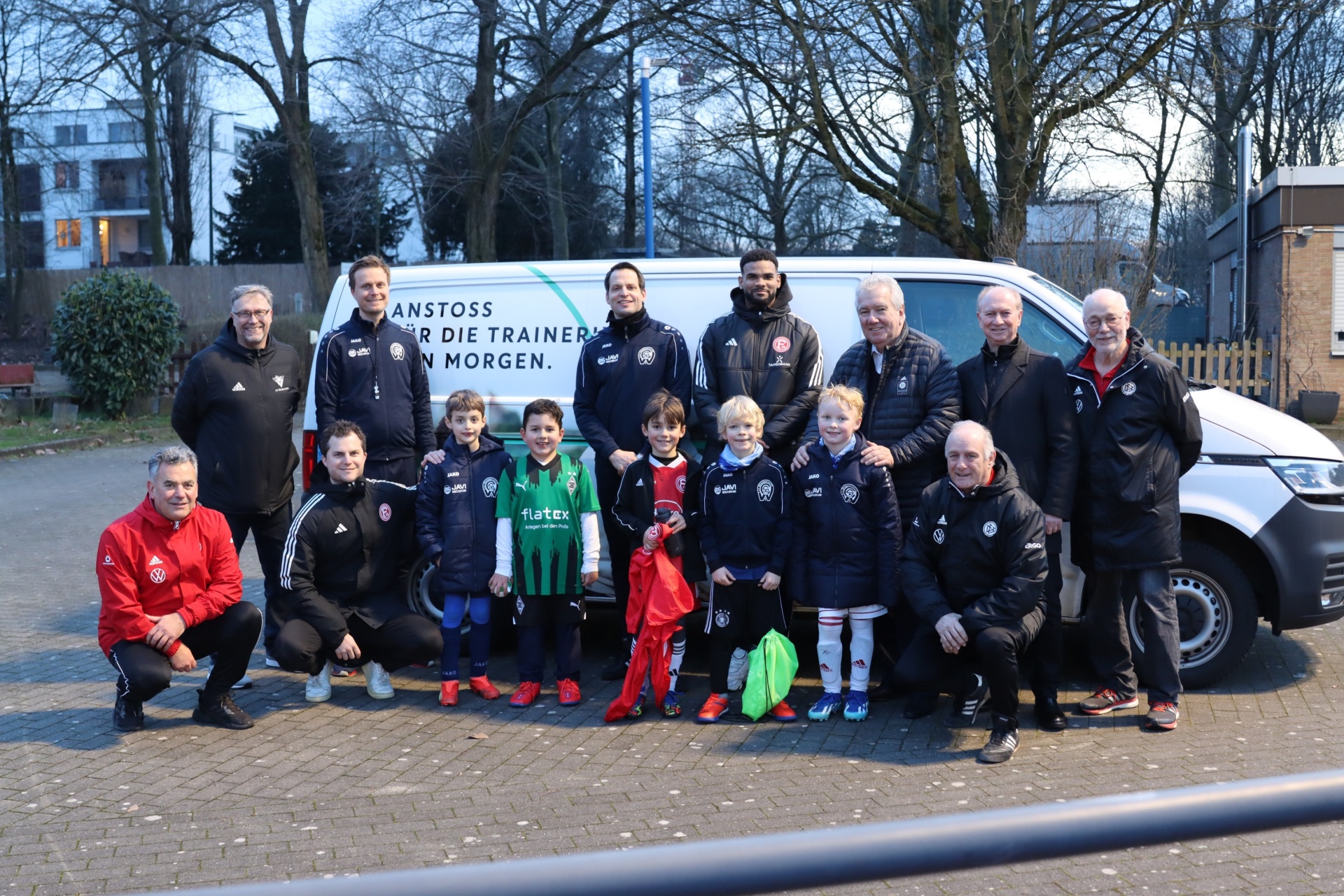 [{"clang_id":1,"value":"Fußballmannschaft mit Trainern vor einem weißen Lieferwagen. Kinder und Erwachsene stehen oder sitzen lächelnd für ein Gruppenfoto."}]