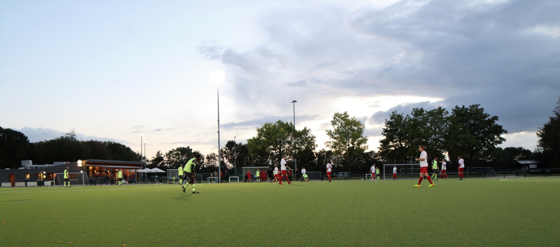 [{"clang_id":1,"value":"Fußballfeld mit spielenden Personen in roten und schwarzen Trikots. Im Hintergrund Bäume und ein bewölkter Himmel."}]