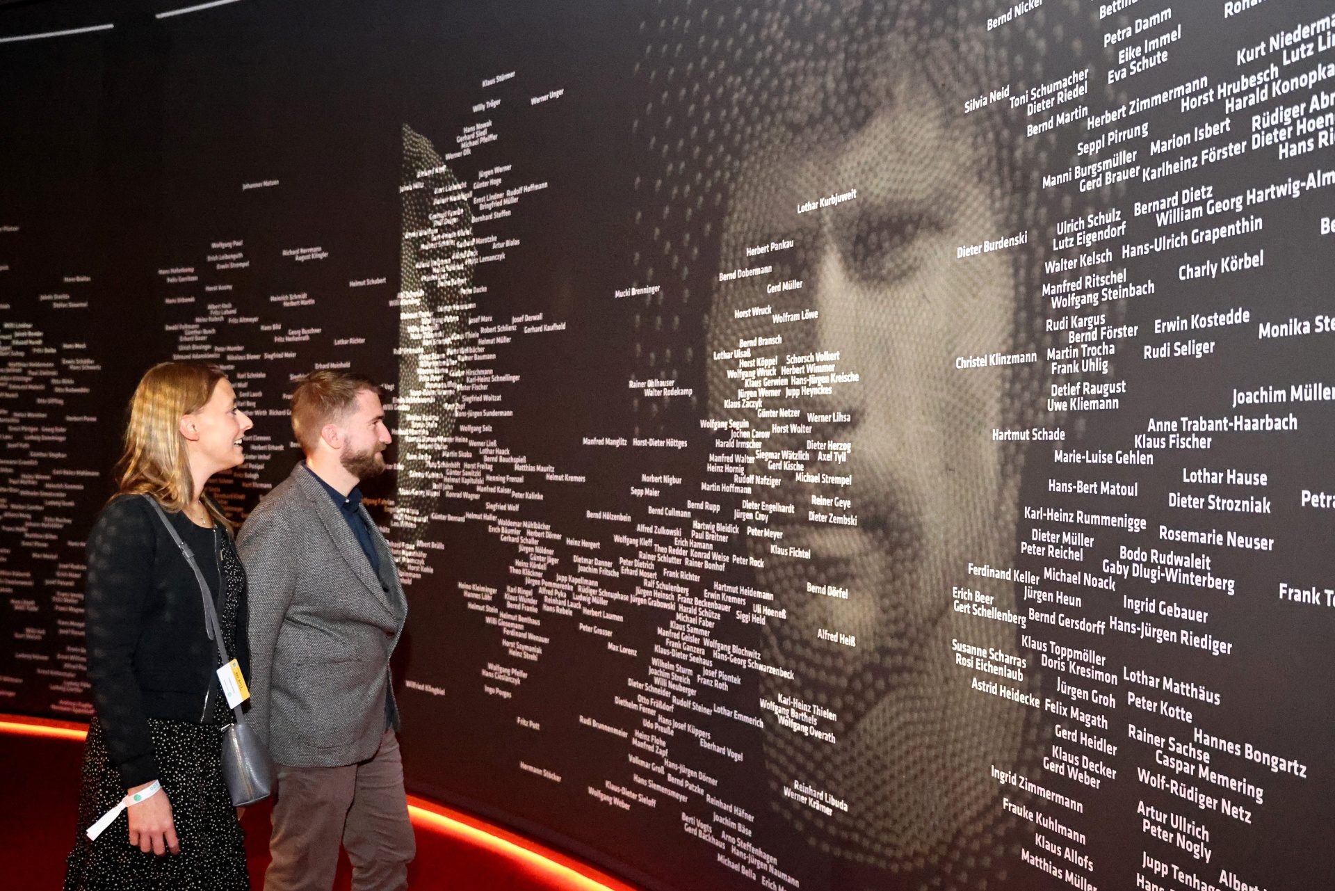 [{"clang_id":1,"value":"Gedenkstätte mit dunkler Wand, bedeckt mit vielen weißen Namen. Im Vordergrund eine Person, die die Namen betrachtet."}]