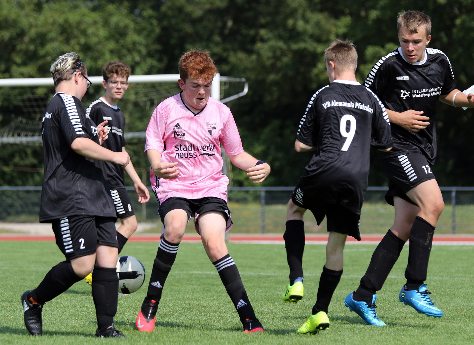 [{"clang_id":1,"value":"Fußballspiel. Mehrere Spieler in schwarzen und pinken Trikots kämpfen um den Ball auf einem grünen Rasenplatz."}]