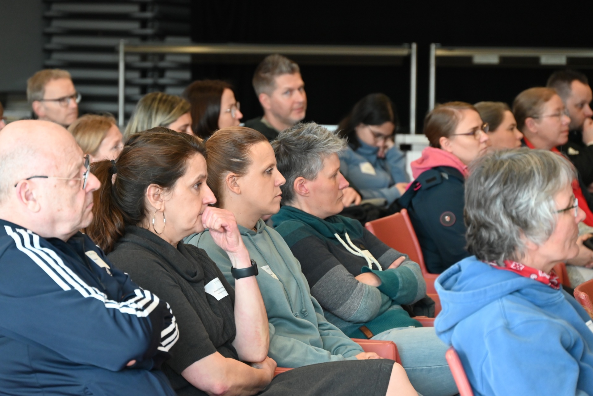 [{"clang_id":1,"value":"Zuschauerreihe in einem Auditorium. Verschiedene Personen sitzen auf roten Sitzen und schauen nach vorne. Unterschiedliche Altersgruppen und Kleidung."}]