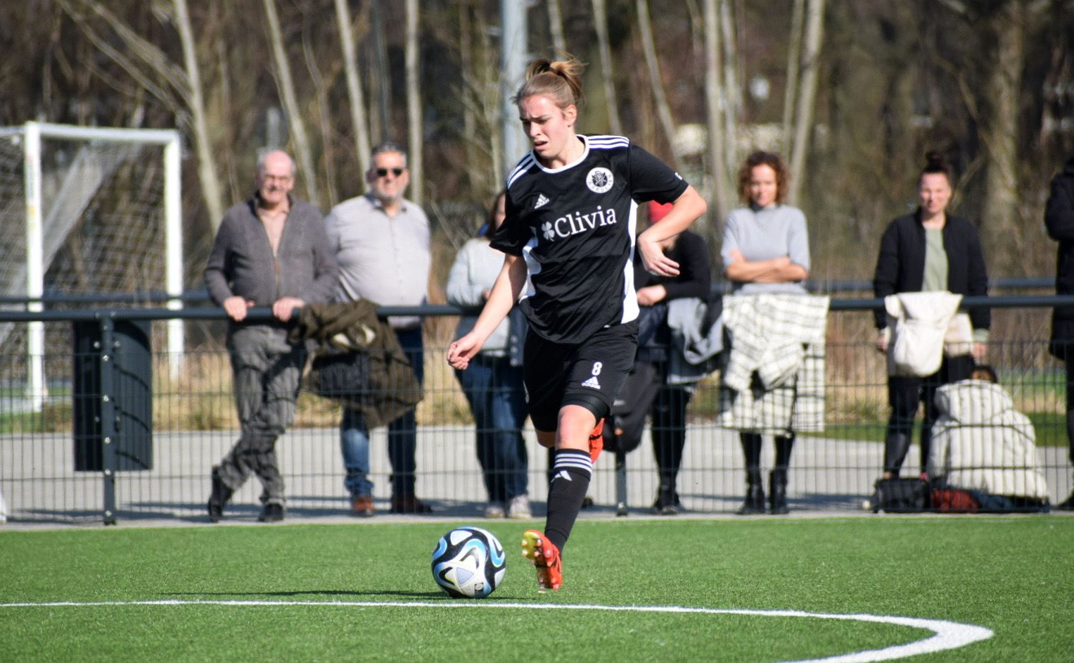 [{"clang_id":1,"value":"Fußballspielerin mit blonden Haaren dribbelt auf grünem Rasen, Zuschauer im Hintergrund."}]