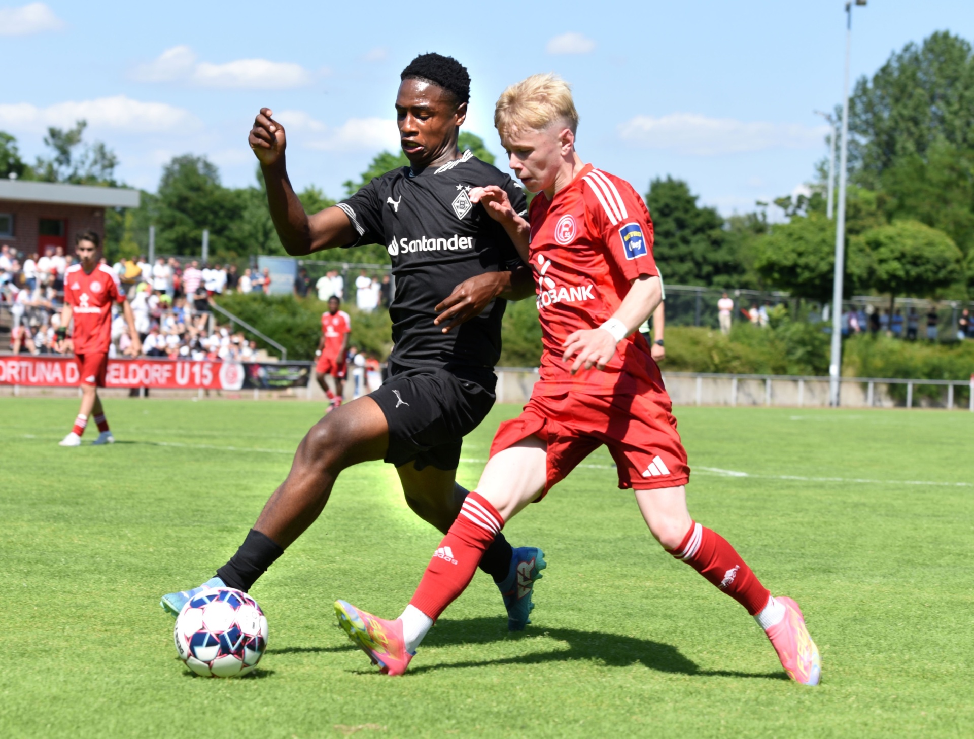 [{"clang_id":1,"value":"Zwei jugendliche Fußballspieler im Zweikampf auf grünem Rasen. Links Spieler mit schwarzem Trikot, rechts mit rotem Trikot. Zuschauer im Hintergrund."}]