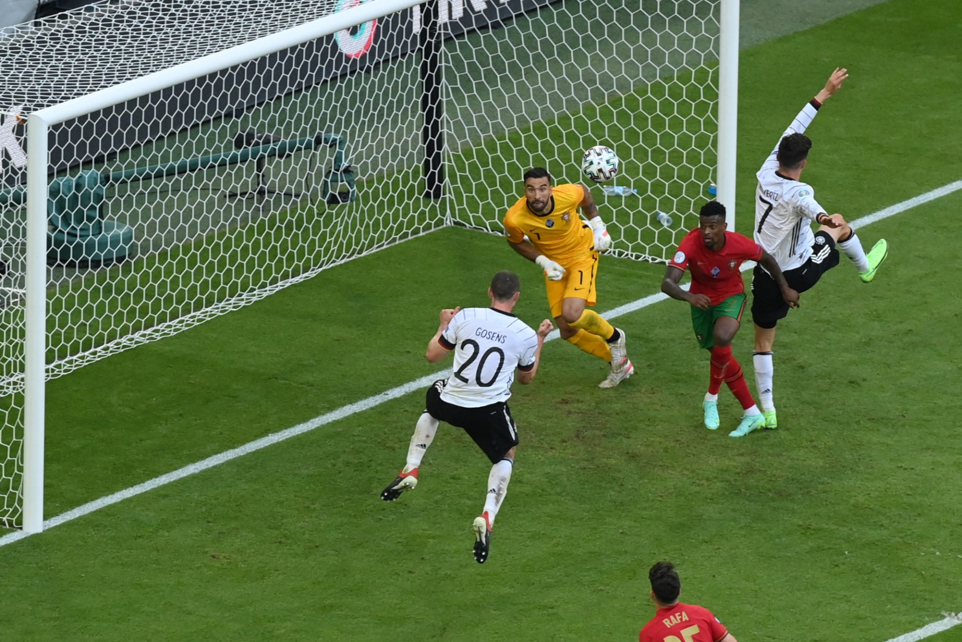 [{"clang_id":1,"value":"Fußballspiel: Torwart in gelbem Trikot versucht, Schuss eines Spielers in weißem Trikot zu halten. Zwei weitere Spieler stehen im Strafraum. Rasen im Vordergrund."}]