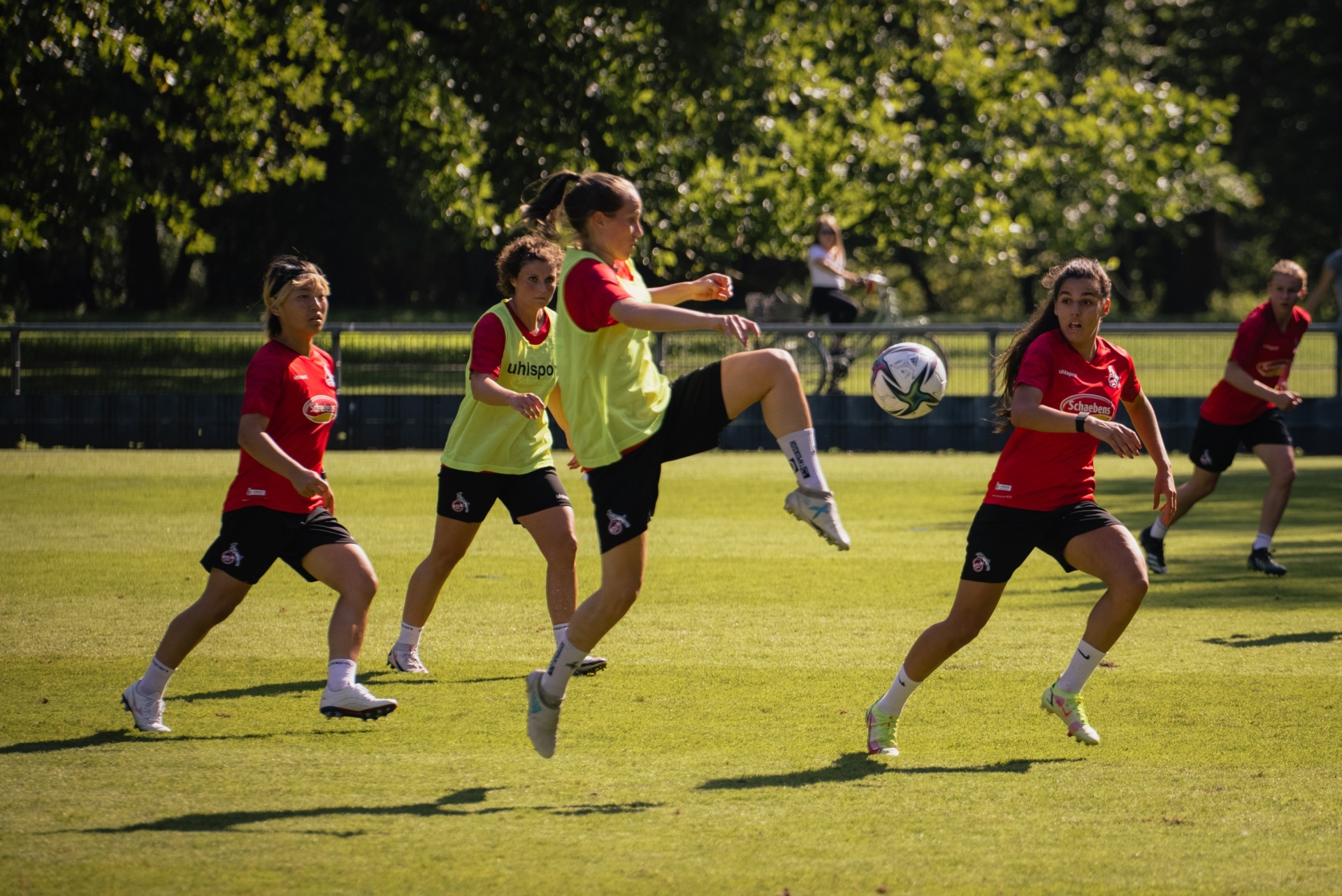 [{"clang_id":1,"value":"Fußballspielerinnen trainieren auf grünem Rasen. Eine Spielerin schießt den Ball, während zwei weitere ihr folgen. Im Hintergrund weitere Spielerinnen und Bäume."}]