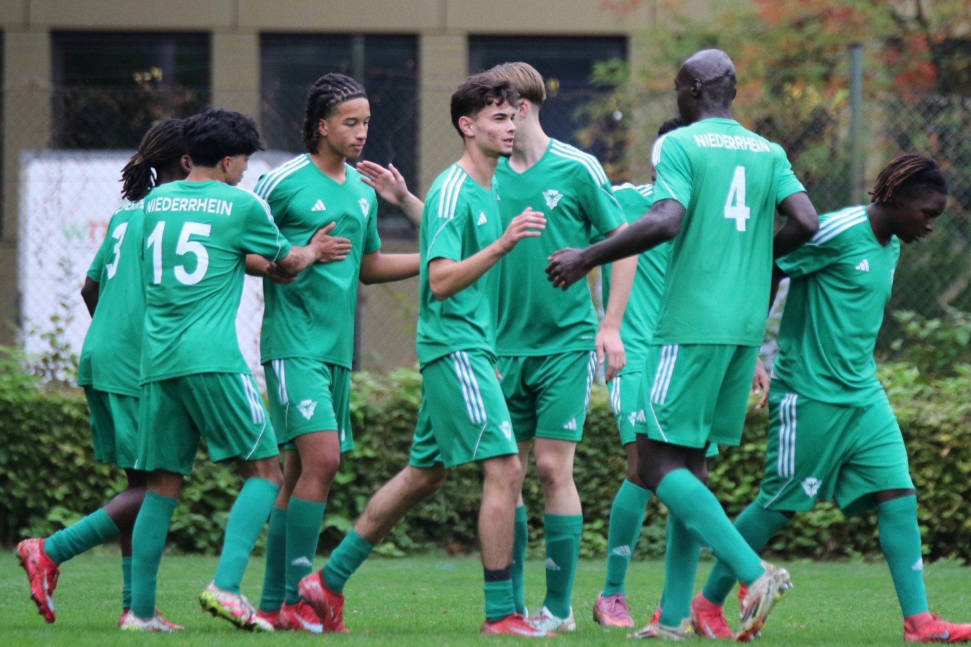 [{"clang_id":1,"value":"Fünf Fußballspieler in grünen Trikots und Shorts feiern auf einem Rasenplatz. Auf den Trikots ist \"NIEDERRHEIN\" zu lesen. Nummer 15 und 4 sind erkennbar."}]
