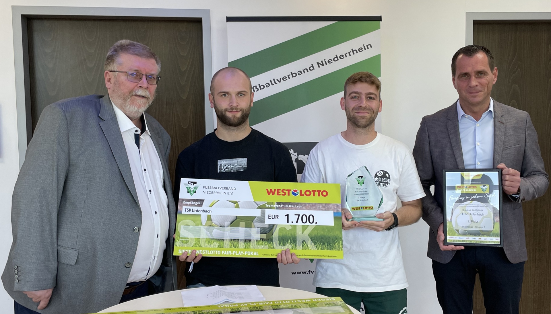 [{"clang_id":1,"value":"Drei Männer stehen für ein Foto zusammen. Sie halten Schecks und Urkunden in den Händen. Im Hintergrund ein Banner mit dem Schriftzug \"Fußballverband Niederrhein\"."}]