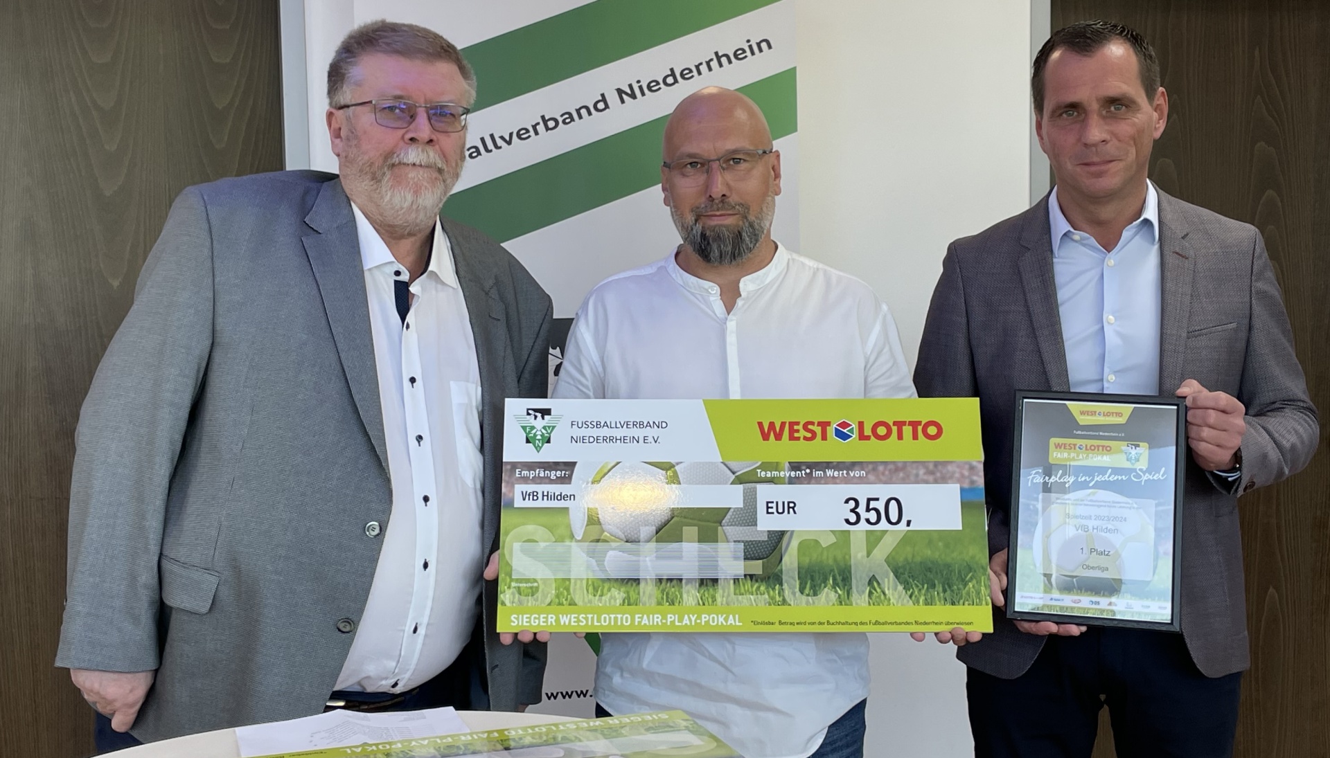 [{"clang_id":1,"value":"Drei Männer im Anzug stehen nebeneinander und halten einen Scheck über 350 Euro sowie eine Urkunde. Im Hintergrund ein Banner mit Fussballverband und Westlotto-Logo."}]