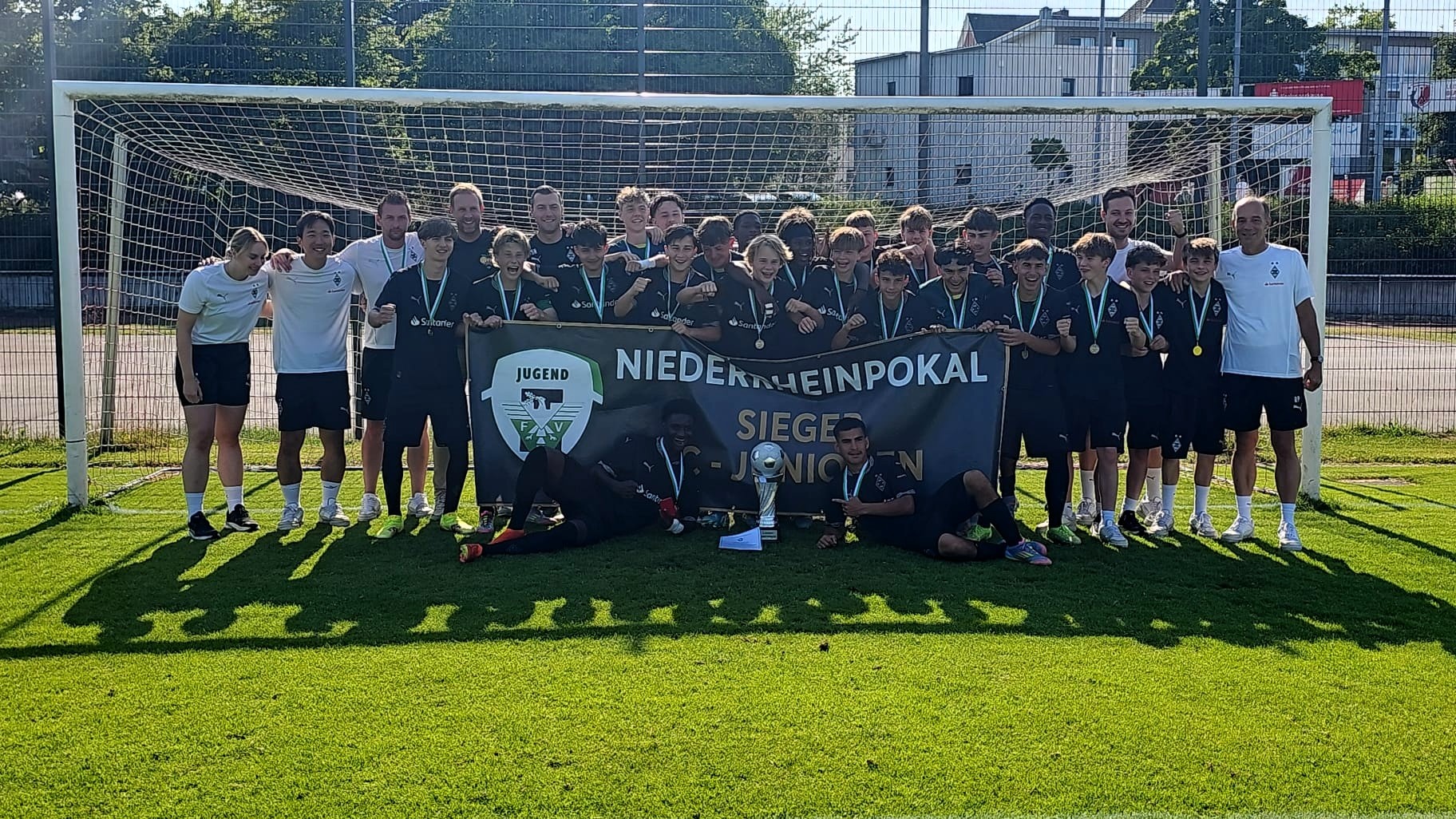 [{"clang_id":1,"value":"Fußballmannschaft mit Medaillen vor einem Tor. Banner mit der Aufschrift \"Niederrheinpokal Jugend\". Grasfläche und Gebäude im Hintergrund."}]