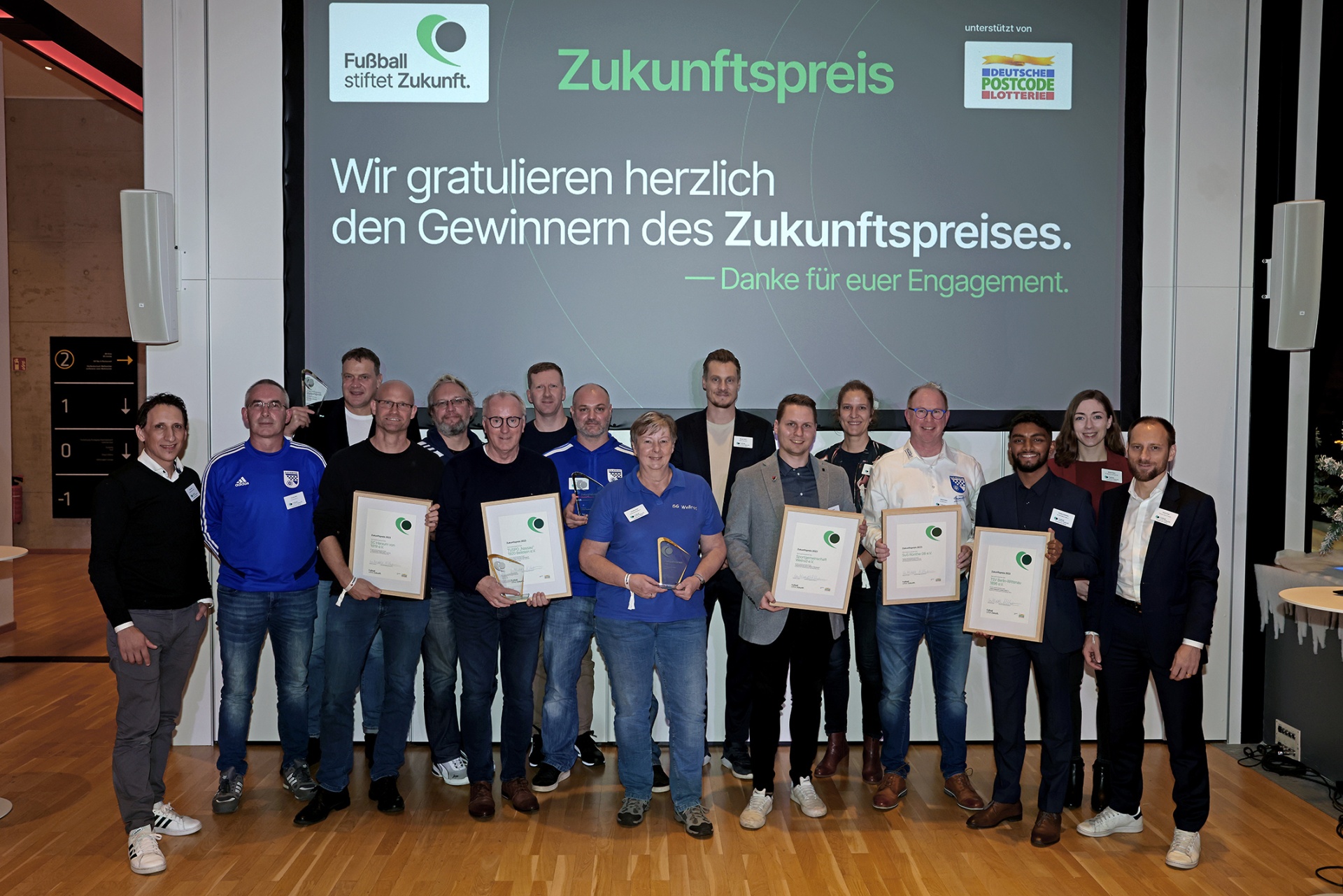 [{"clang_id":1,"value":"Gruppe von Personen mit Urkunden vor Banner mit Aufschrift \"Zukunftspreis\". Im Hintergrund ein Treppenhaus und eine Pflanze."}]