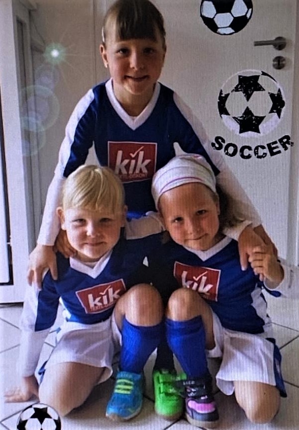 [{"clang_id":1,"value":"Drei Kinder in blauen Fußballtrikots mit weißem Logo \"kik\" und weißen Shorts stehen vor einer Tür mit Fußballmotiven."}]