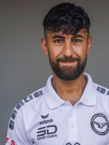 [{"clang_id":1,"value":"Mann mit dunklem, lockigem Haar und Bart trägt weißes Poloshirt mit Logo \"Erima\" und \"Sport Duwe\". Hintergrund ist ein grauer Farbverlauf."}]