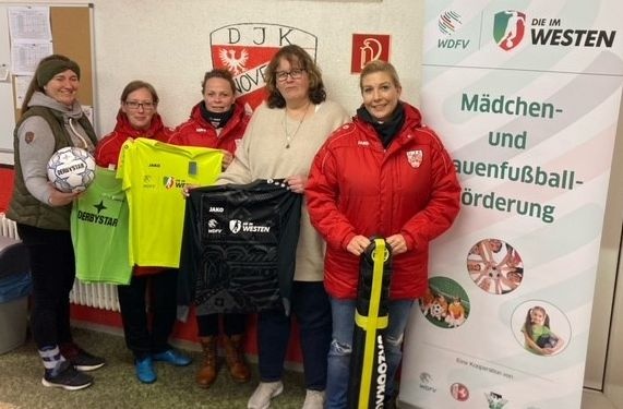 [{"clang_id":1,"value":"Fünf Frauen stehen lächelnd in einer Sporthalle. Sie halten Fußbälle, Trikots und einen Fußpump. Im Hintergrund ein Banner mit Fußballmotiven und Schrift."}]