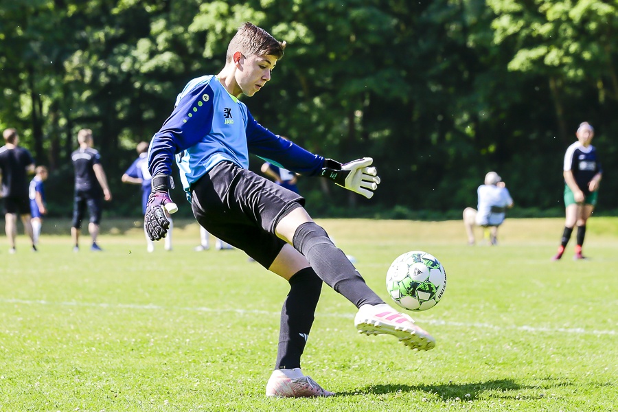 [{"clang_id":1,"value":"Fußballtorwart in blau-gelbem Trikot schießt Ball auf grünem Rasen. Im Hintergrund weitere Spieler und Bäume."}]