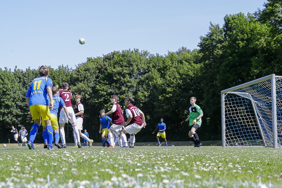 [{"clang_id":1,"value":"Fußballspiel auf grünem Rasen mit vielen Spielern in bunten Trikots. Der Ball ist in der Luft, ein Torwart steht bereit. Bäume im Hintergrund."}]