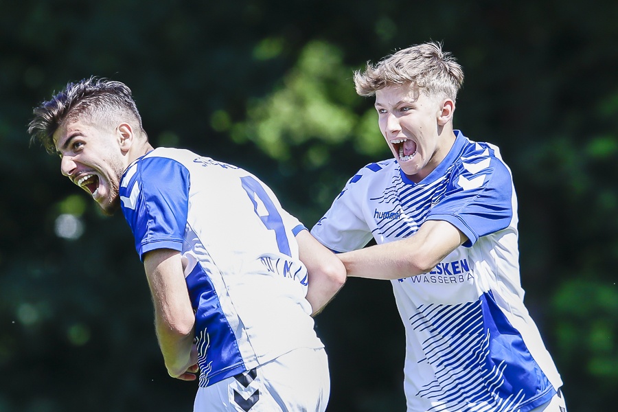 [{"clang_id":1,"value":"Zwei Fußballspieler in blauen Trikots jubeln vereint, Arm in Arm, auf einem grünen Rasen. Beide schreien und zeigen Emotionen."}]