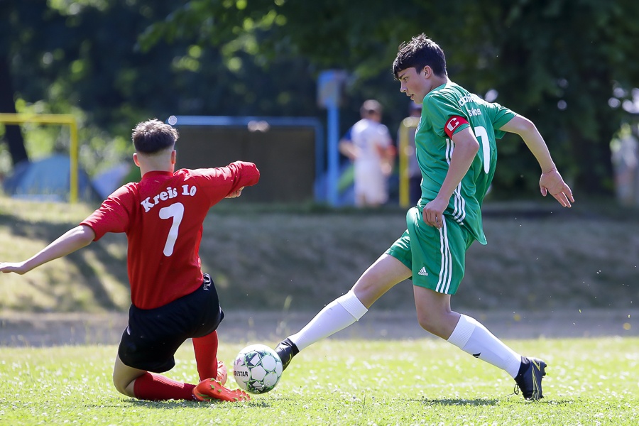 [{"clang_id":1,"value":"Zwei Fußballspieler auf grünem Rasen. Links ein Spieler in rotem Trikot mit Nummer 7, rechts ein Spieler in grünem Trikot, der den Ball schießt. Im Hintergrund Zuschauer und Bäume."}]