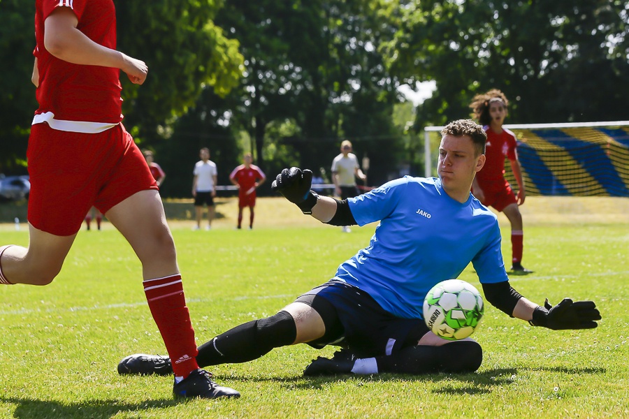 [{"clang_id":1,"value":"Fußballtorwart in blau rutscht grasbewachsenem Feld entgegen, um Ball zu halten. Im Hintergrund Spieler in rot und Zuschauer."}]