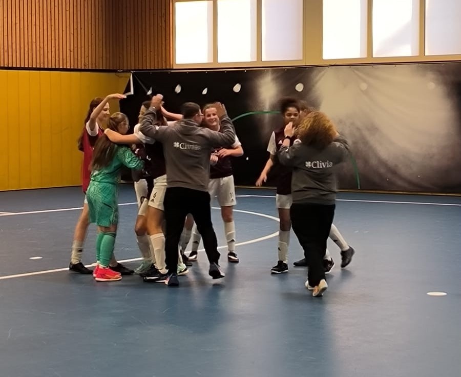 [{"clang_id":1,"value":"Gruppe von jungen Sportler*innen in Sporthalle, feiert gemeinsam mit erhobenen Armen und engem Kreis. Tragen Sportkleidung in verschiedenen Farben."}]