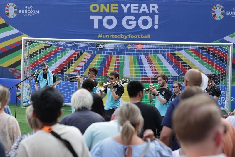 [{"clang_id":1,"value":"Fußballtor mit Spruch \"One Year to Go!\". Band spielt davor, Publikum im Hintergrund. UEFA Euro 2024 Deutschland Logo."}]
