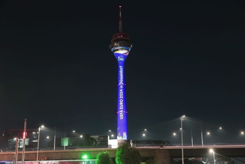 [{"clang_id":1,"value":"Nachts erleuchteter Fernsehturm in Düsseldorf. Vertikal angebracht steht \"UEFA EURO 2024 in Düsseldorf\". Darunter befindet sich eine Straße und Vegetation."}]