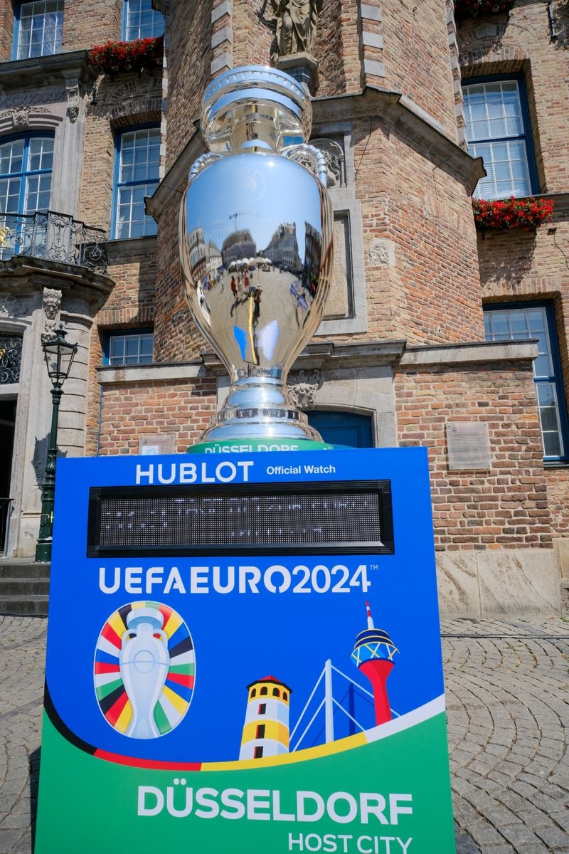 [{"clang_id":1,"value":"UEFA Euro 2024 Pokal auf einer Werbetafel in Düsseldorf. Im Hintergrund ein historisches Gebäude mit Balkonen und Blumenkästen."}]