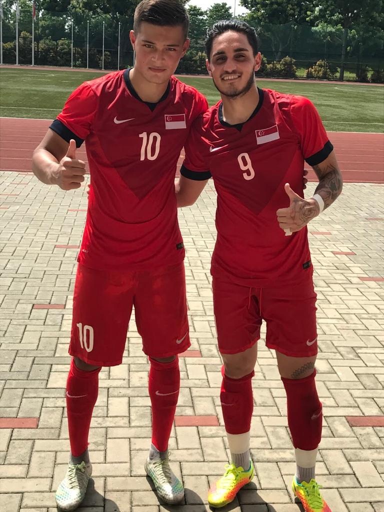 [{"clang_id":1,"value":"Zwei Fußballspieler in roten Trikots mit den Nummern 10 und 9 stehen nebeneinander und zeigen mit dem Daumen nach oben. Im Hintergrund eine Laufbahn und Grünfläche."}]