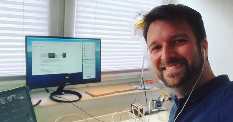 [{"clang_id":1,"value":"Mann lächelt in die Kamera, sitzt vor Computer mit geöffnetem Fenster. Hinter ihm ein Fenster mit Jalousien und ein Schreibtisch."}]