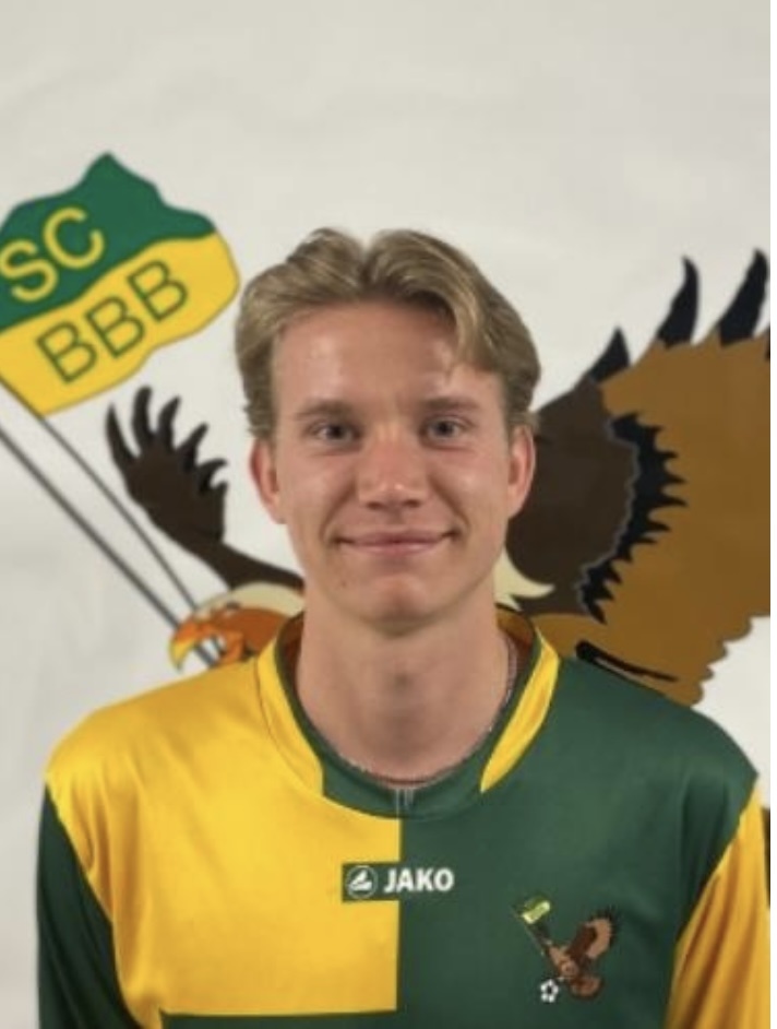 [{"clang_id":1,"value":"Handballspieler mit blonden Haaren in grün-gelbem Trikot, Logo \"SC BBB\" und Adler-Motiv im Hintergrund."}]