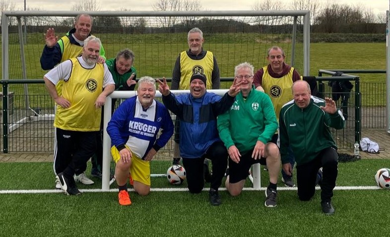 [{"clang_id":1,"value":"Fußballmannschaft posiert lächelnd auf Kunstrasenfeld vor einem Fußballtor. Spieler tragen Trainingsanzüge und Westen. Zwei Fußbälle liegen vor der Gruppe."}]